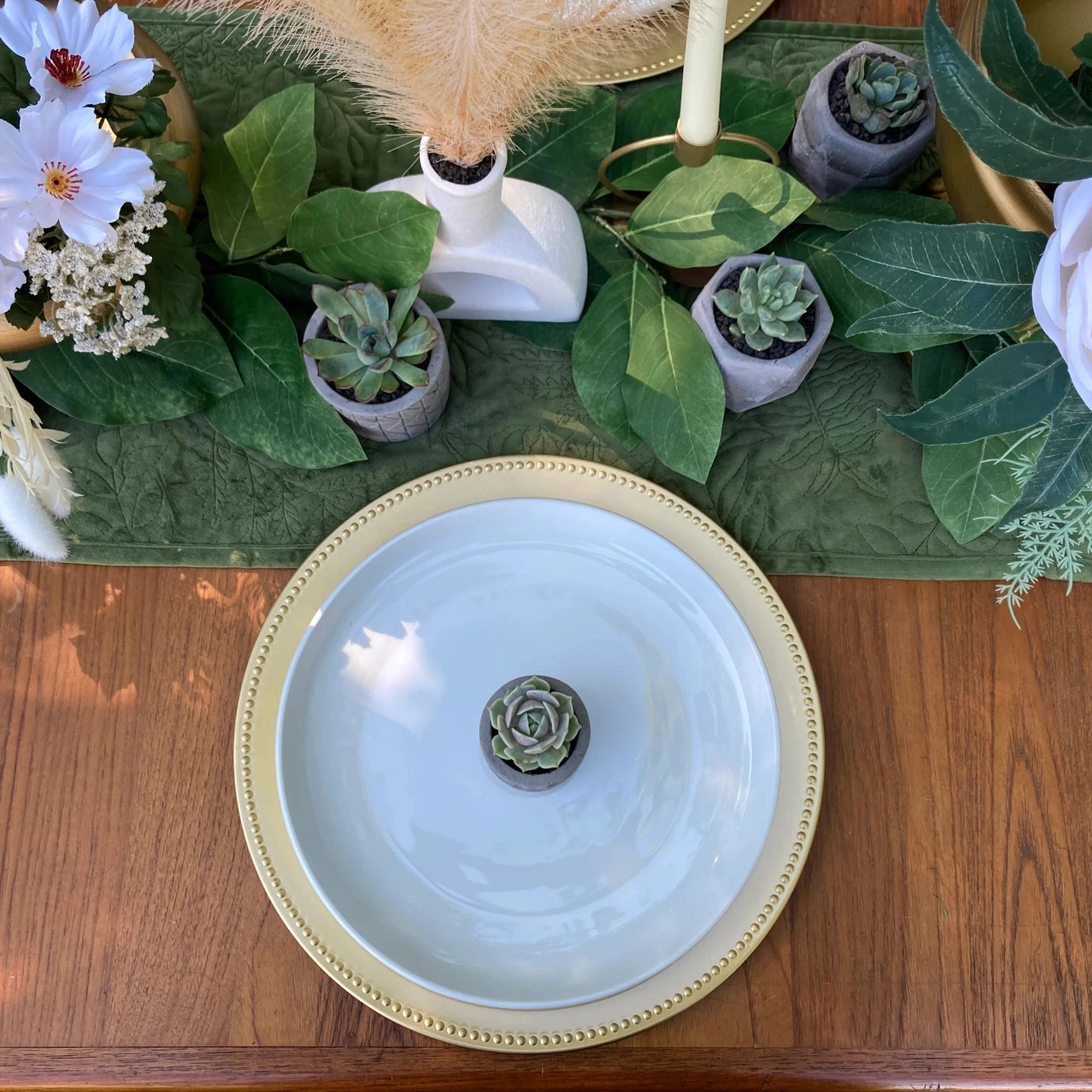 An aerial view of a gold place setting with a succulent in the center of the dinner plate and succulents surrounding.